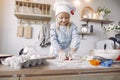 Little girl in a white shef hat cook the dough for cookies