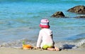 Sad little girl in a white shirt sits on the shore lonely plays with toys on the beach looks at the waves of the sea Royalty Free Stock Photo