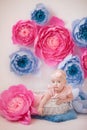 Little girl in a white suit in a white room with bright pink and blue paper flowers, baby photo session Royalty Free Stock Photo