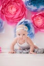 Little girl in a white suit in a white room with bright pink and blue paper flowers, baby photo session