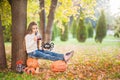 Little girl in a white sweater and jeans on a background of green textural natural background. A girl sits on pumpkins and drinks Royalty Free Stock Photo