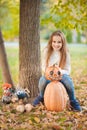 Little girl in a white sweater and jeans on a background of green textural natural background. The girl sits on pumpkins and laugh Royalty Free Stock Photo