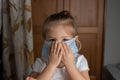 Little girl  in a white T-shirt covers her face with her hands in a medical mask at home Royalty Free Stock Photo