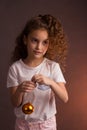 A little girl in a white t-shirt with curly long hair, holding a ball of Christmas tree decoration, looks away on a dark purple Royalty Free Stock Photo