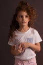 A little girl in a white t-shirt with curly long hair, holding a ball of Christmas tree decoration, looks away on a dark purple Royalty Free Stock Photo