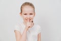 Little girl with in a white T-shirt holds index finger in front of lips