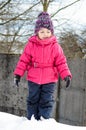 Little girl in winter clothes is playing in snow with snow on he