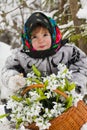 Little girl in a winter wood with the big basket of snowdrops