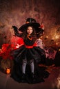 A little girl in a witch costume on a gloomy background scares people. Getting ready for All Saints Day. Halloween costume