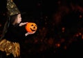 A little girl in a witch costume, holding a pumpkin, shot on a black background. Happy Halloween concept. Royalty Free Stock Photo