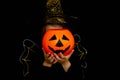 A little girl in a witch costume, holding a pumpkin, shot on a black background. Happy Halloween concept. Royalty Free Stock Photo