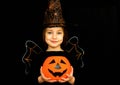 A little girl in a witch costume, holding a pumpkin, shot on a black background. Happy Halloween concept. Royalty Free Stock Photo