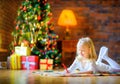 Little girl writes a letter to santa lying on the floor near Christmas tree