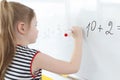 Little girl writes math examples on white board Royalty Free Stock Photo