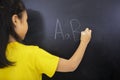 Little girl writing alphabet letters on the blackboard