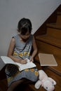 Little girl writing book and having cookie at stairway at home Royalty Free Stock Photo