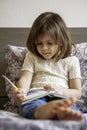 Little girl writing on the diary or paper notebook sitting on bed at home. Cute little girl in casual wearing is engaged with Royalty Free Stock Photo