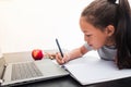 Little girl writing on a notebook, taking class from the laptop on white background. Concept of online classes at home during the Royalty Free Stock Photo