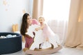 A little girl of 1 year in a pink dress is sitting on a wooden horse, she is happy and smiling. Her mother is sitting on the floor Royalty Free Stock Photo