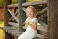 Little girl 5 years blonde sitting on a log home, holding hands