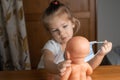 a little girl of 4 years old plays with a baby doll at home, puts a medical mask on a doll