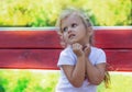 Little girl 4 years old, sitting on a park bench with an unhappy expression on her face, with anxiety in her eyes, pressing her ha Royalty Free Stock Photo