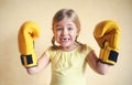 Little girl with yellow boxing gloves over yellow wall background. Girl power concept