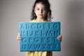 Little girl with yellow dress holding an English letters sheet in hands Royalty Free Stock Photo