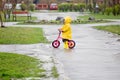 little girl in yellow raincoat rides on bike ride through puddles in rain. Rainy weather in spring. child learns to Royalty Free Stock Photo