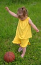 Little girl in yellow suit plays ball on lawn