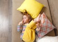 a little girl in yellow trousers and a bright T-shirt is lying on her back on the sofa with her legs up, biting her