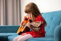 Little girl, young school age child playing an acoustic guitar, practicing a musical instrument sitting on a sofa at home Royalty Free Stock Photo