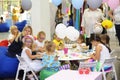 Little girls and adults sitting at tables painting at children lounge zone of a shopping mall.