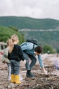 Little girls with bags look at their mother collecting trash on the beach. Back view Royalty Free Stock Photo