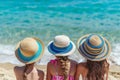 little girls in beautiful straw hats sit on the sand and look at the sea. girl friends are relaxing at sea. bright sunny day.