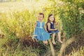 2 little girls in blue dress on swing in summertime on field. Happy children playing outdoors in sunset in summer. Cheerful and