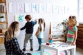 Little girls and educator looking at boy showing pictures on wall in playroom. Interesting logic and intelligence lesson