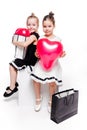 2 little girls with elegant dresses sit with large bags with heart-shaped balloons inside Royalty Free Stock Photo