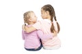 Little girls girlfriends in jeans and pink sweaters are sitting and hugging. Isolated over white background