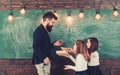 Little girls listen to bearded man at school board. Teacher write with chalk on chalkboard. Tutor teach children Royalty Free Stock Photo