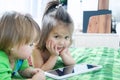 Little girls looking on pad lying on bed. Children time spending. Kids using tablet computer