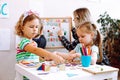 Little girls playing with cubes and geometric figures on desk in playroom, educator with boy studying alphabet on