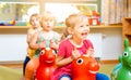 Little girls riding on play horses in kindergarten