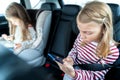 Little girls, sisters are driving in car, children play video games in tablet and mobile phone. Traveling on road in safe baby