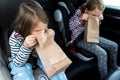 Little girls, sisters are driving in car. Children are sick, vomit into paper bag. Traveling on road in safe baby seats with child