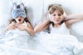 Little girls sleep in bed. One is snoring hard,sister is plugging ears with fur headphones.Early morning wake up,rise to Royalty Free Stock Photo