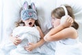 Little girls sleep in bed. One is snoring hard,sister is plugging ears with fur headphones.Early morning wake up,rise to Royalty Free Stock Photo