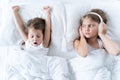 Little girls sleep in bed. One is snoring hard,sister is plugging ears with fur headphones.Early morning wake up,rise to Royalty Free Stock Photo