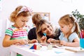 Little girls and smiling educator studying geometric figures, playing and folding cubes on desk sitting on floor in