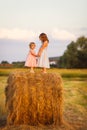 Little girls stand on a hay stack on wheat field